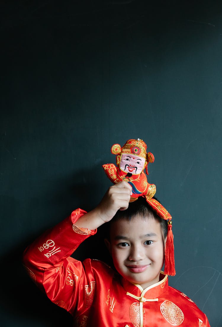 Cute Chinese Kid In Traditional Costume Holding Money Toy And Smiling At Camera