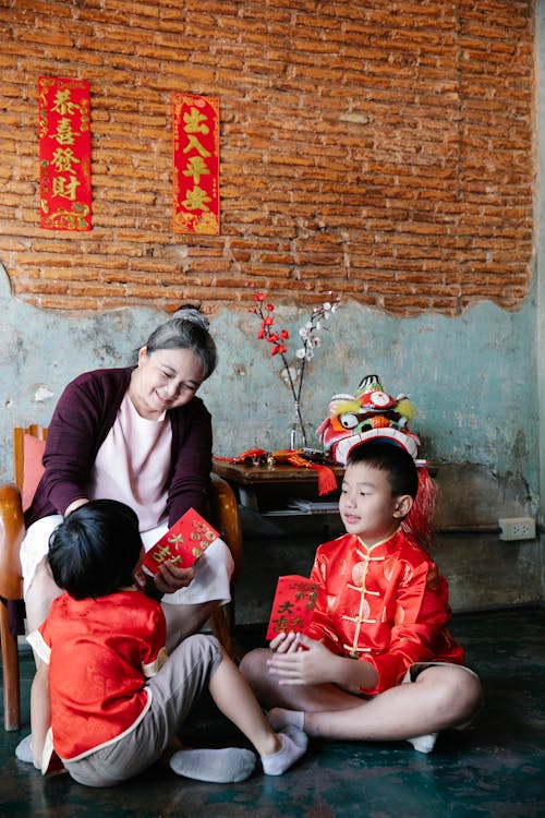 Happy senior ethnic woman gifting red envelopes to grandsons during New Year celebration
