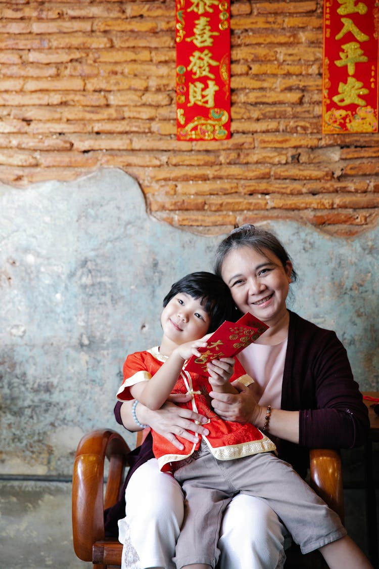 Smiling Mature Asian Woman Embracing Cute Grandson During New Year Celebration