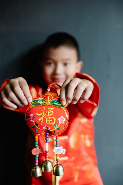 Adorable little Asian boy with dark hair in national costume demonstrating traditional Chinese lucky money bag during New Year celebration