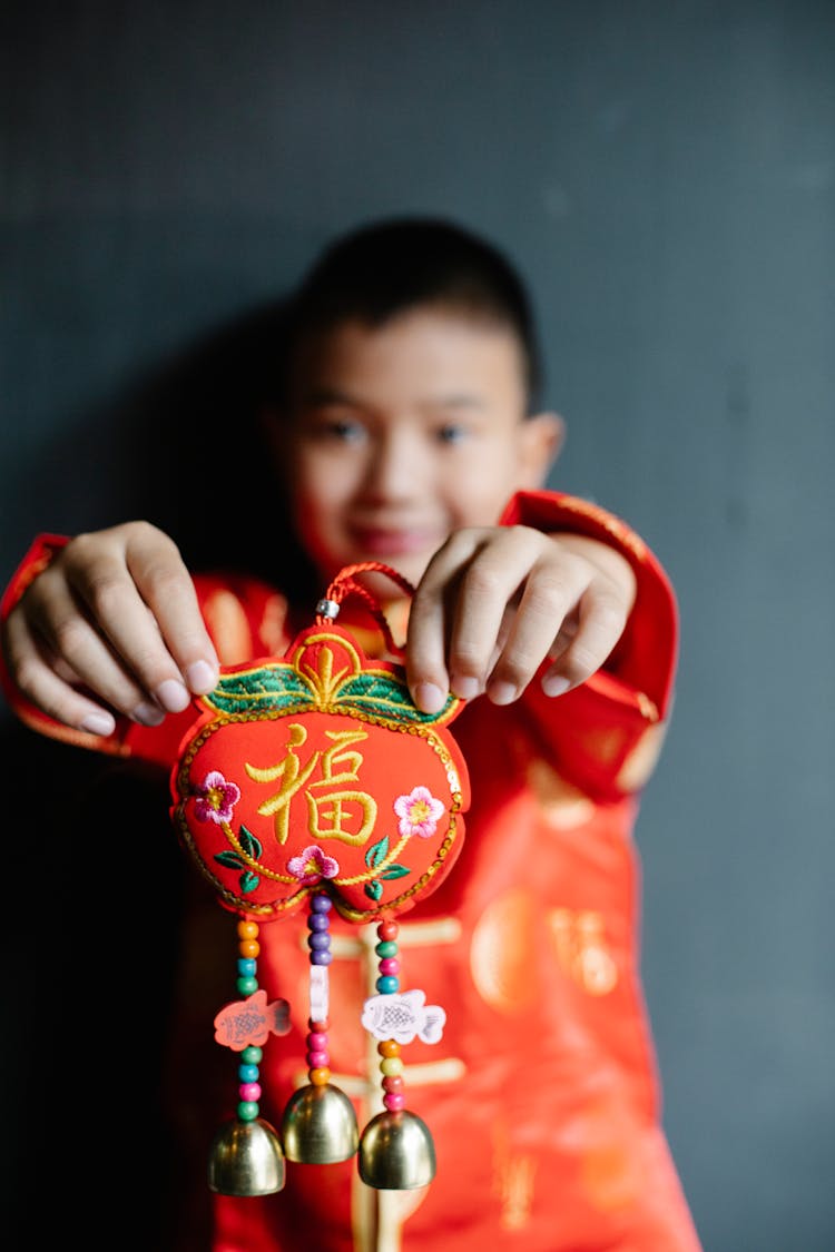 Smiling Ethnic Kid Showing Chinese New Year Decoration Against Black Wall