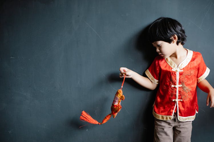 Little Boy In A Traditional Chinese Shirt Holding An Ornament 