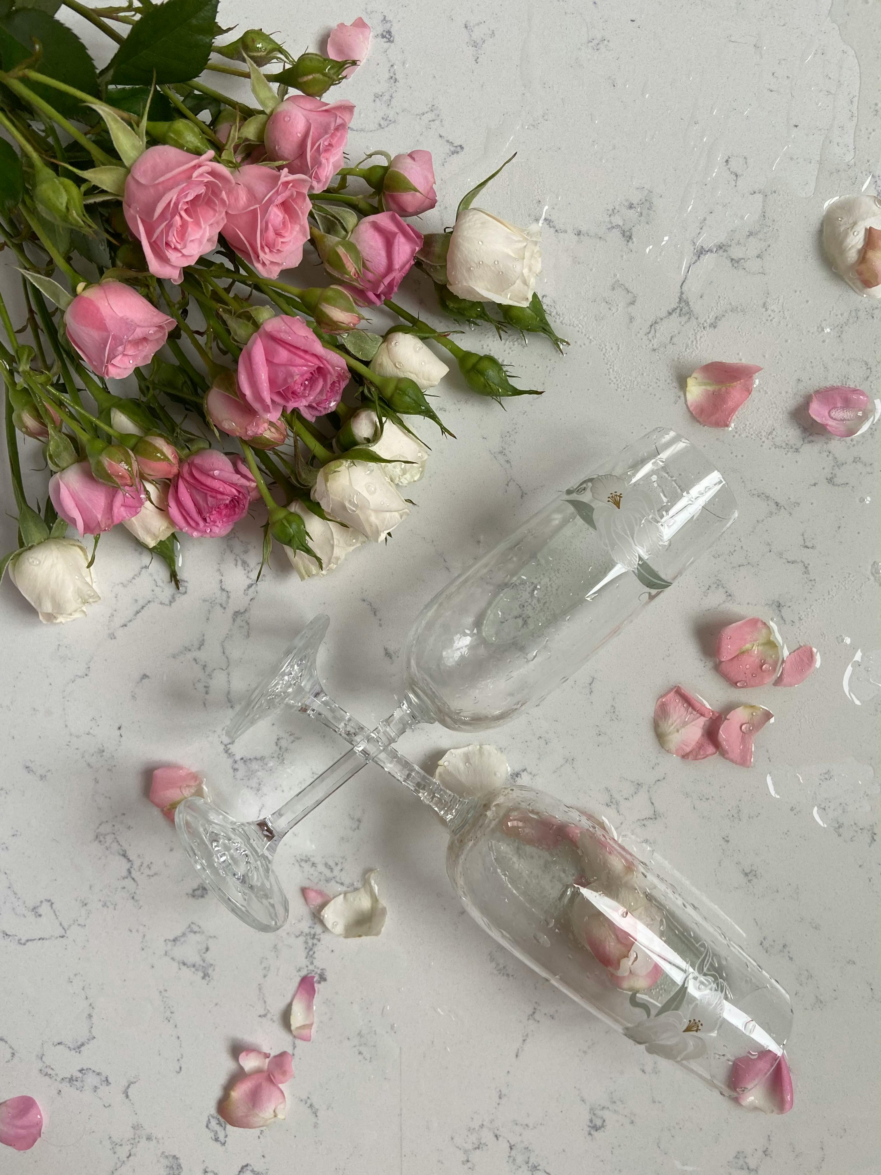 Delicate pink and white roses with champagne glasses on a marble surface.