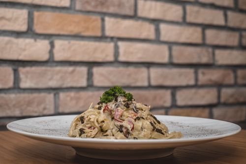 Free Delicious creamy fettuccine pasta garnished with herbs, elegantly plated against a rustic brick wall. Stock Photo