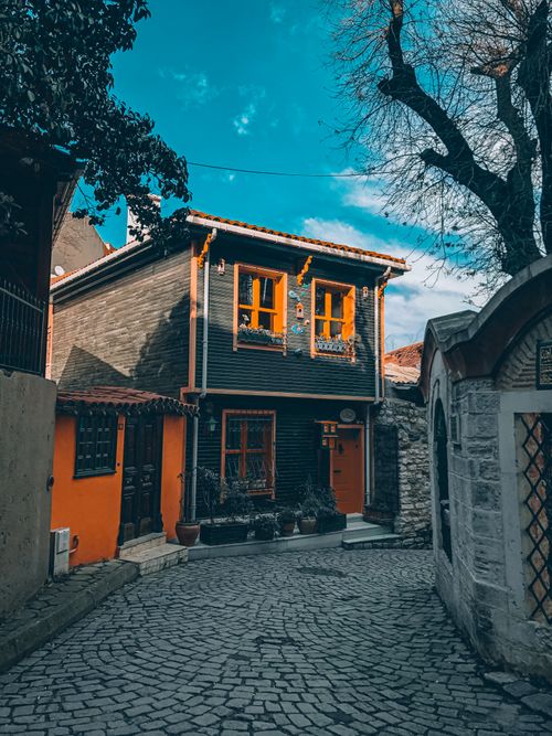 Free A vibrant orange house with wooden facade on a quaint cobblestone street under a clear blue sky. Stock Photo