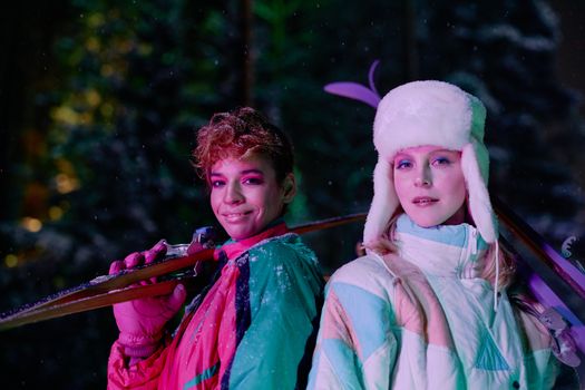 Two fashionable women holding skis, posing at night in winter sportswear with a vibrant style.