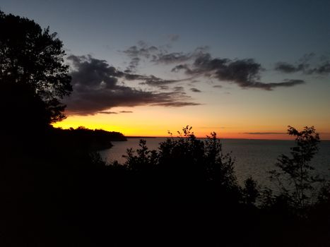 Serene sunset view with vibrant sky and silhouetted trees over a tranquil ocean.