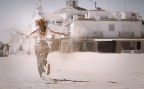 Free Woman Running on Sand Near White Concrete Building Stock Photo