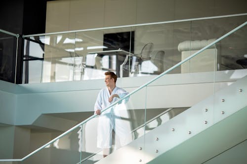 A Man in a Bathrobe Standing Behind the Glass Railing