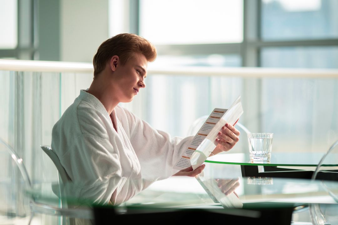 Print Design That Complements Your Hotel's Digital Brand 1 Man in a bathrobe reading a menu at a hotel lounge glass table with refreshing ambiance.