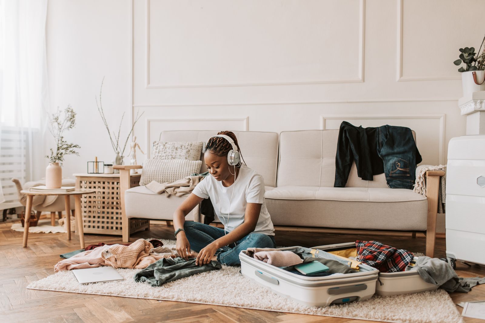 Woman sitting on a living room rug packing clothes into an open white carry-on suitcase