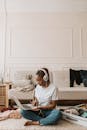 年轻女子与辫子的头发坐在盘腿，工作在一台笔记本电脑和听音乐在一个舒适的客厅