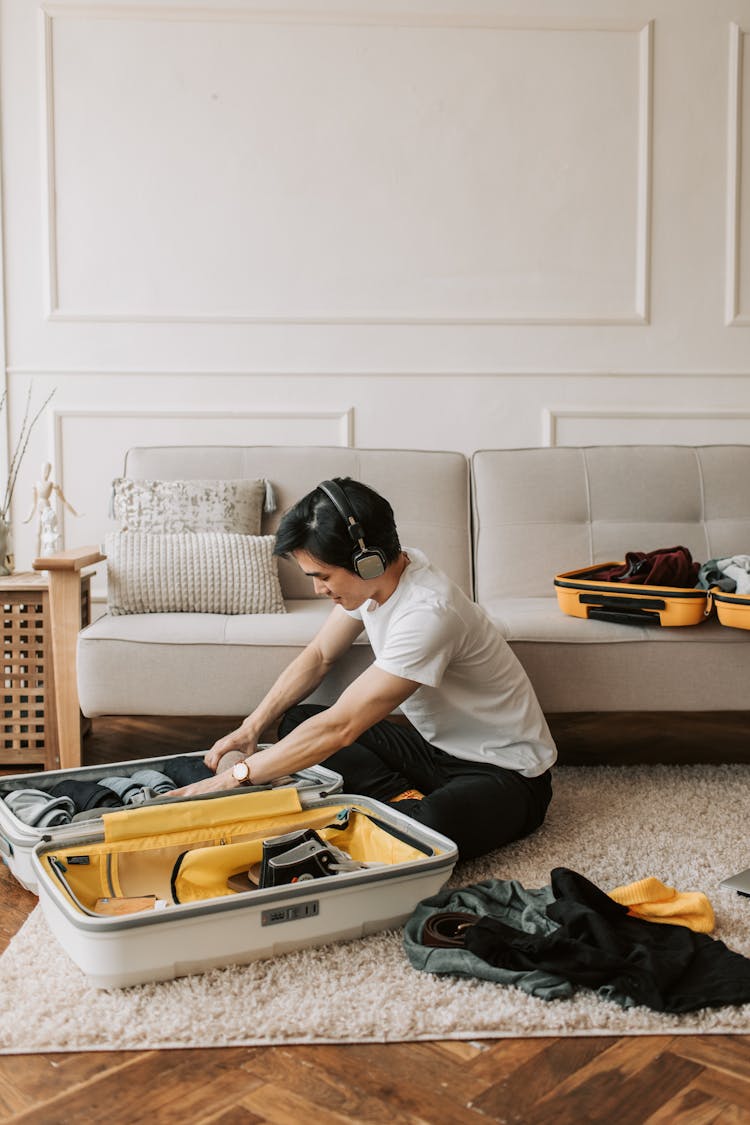 A Man Listening On His Headphones While Packing His Clothes