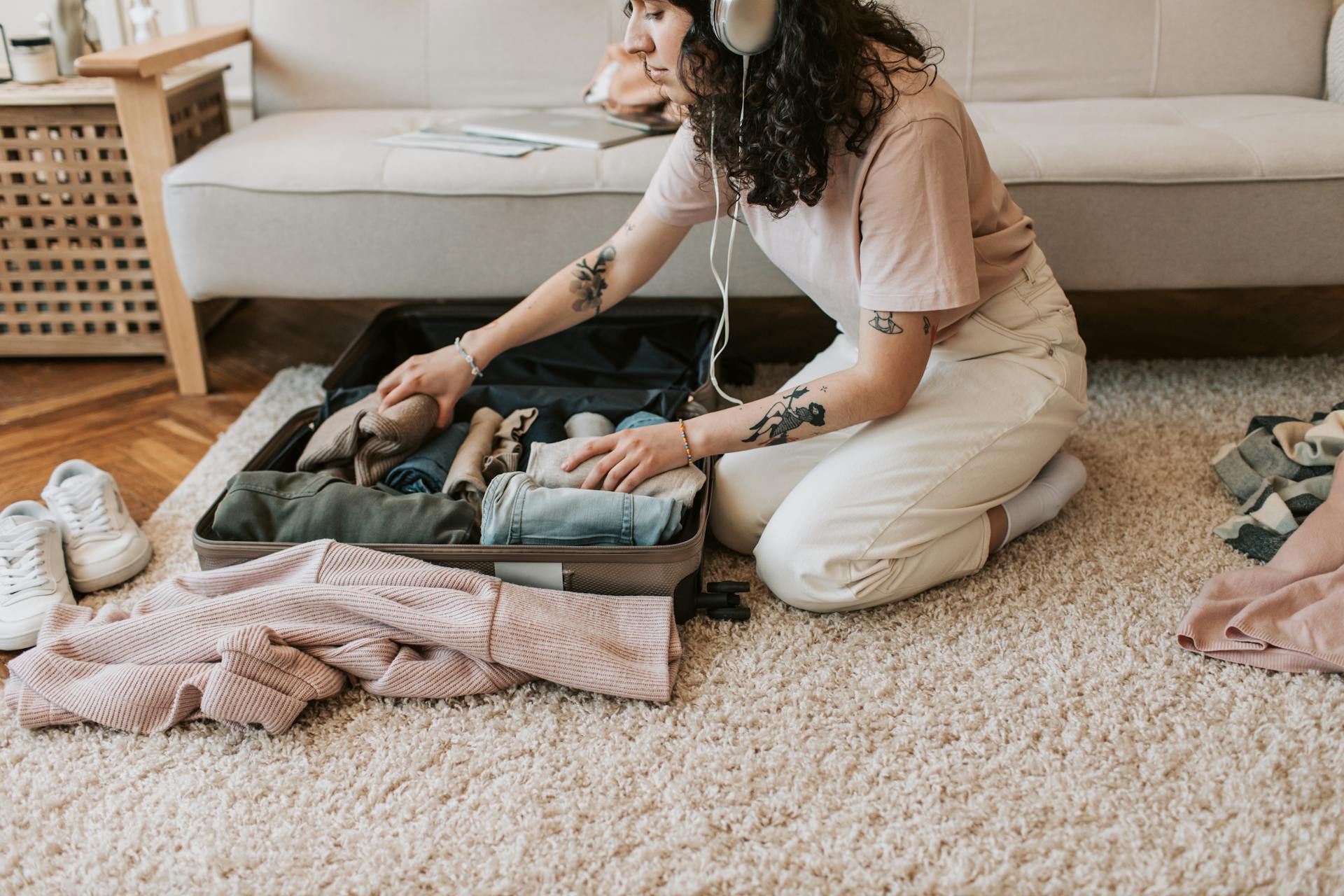 A Woman Listening on Her Headphones while Packing Her Clothes