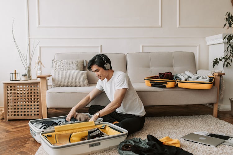 A Man Listening On His Headphones While Packing His Clothes