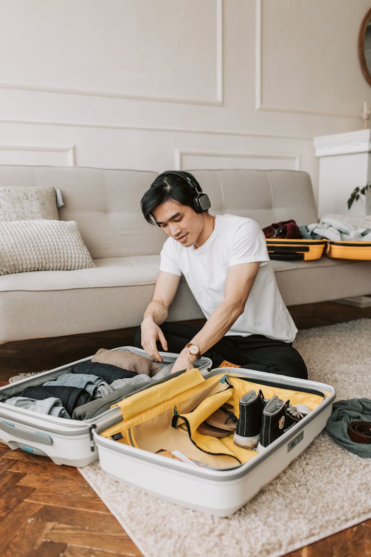 A Man Listening On His Headphones While Packing His Clothes