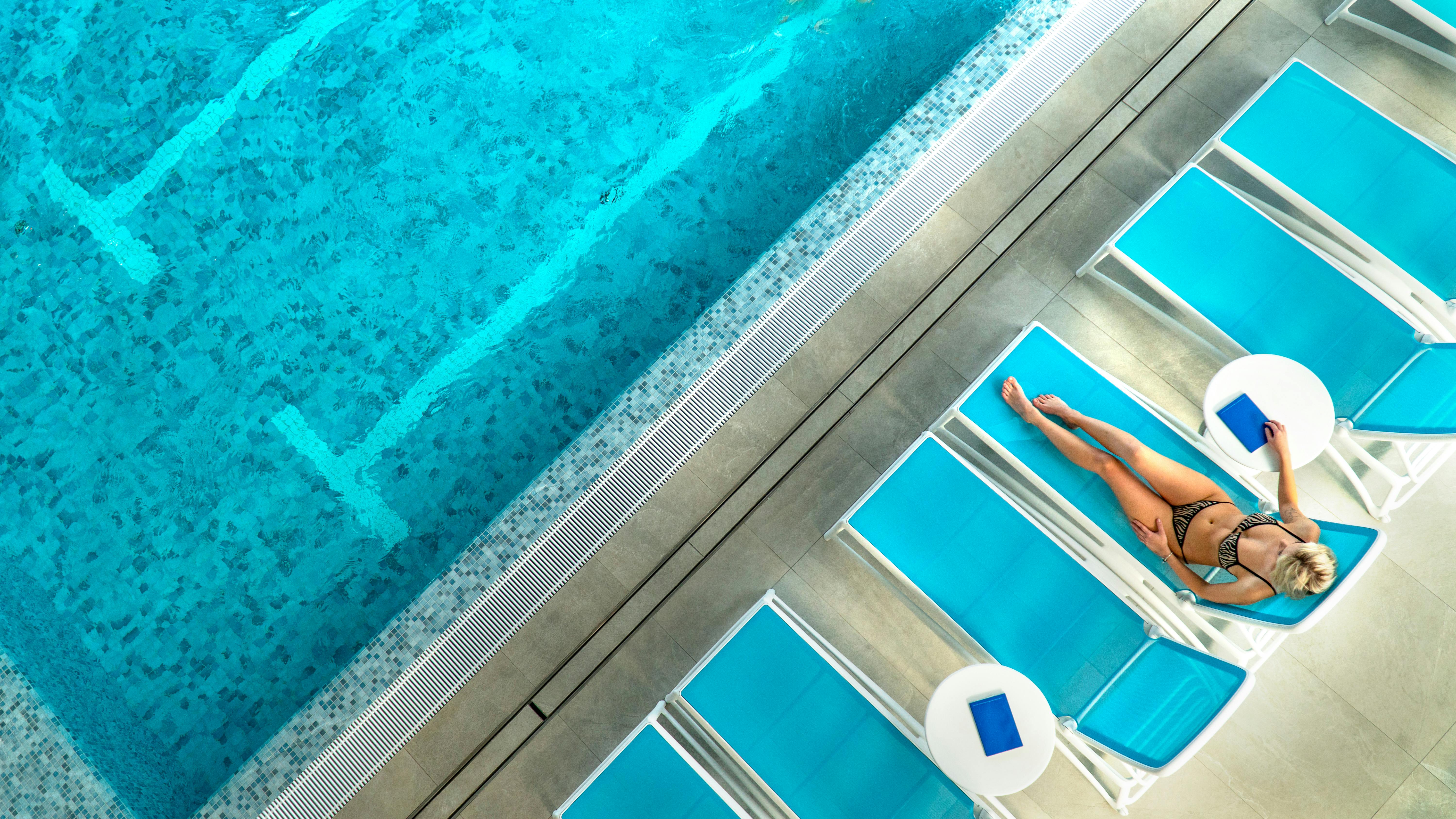 High angle shot of a woman sunbathing by a blue swimming pool on a sunny day.