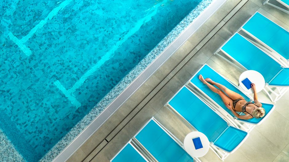 High angle shot of a woman sunbathing by a blue swimming pool on a sunny day.