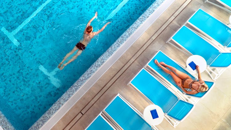 A Woman Resting And A Man Swimming In A Swimming Pool