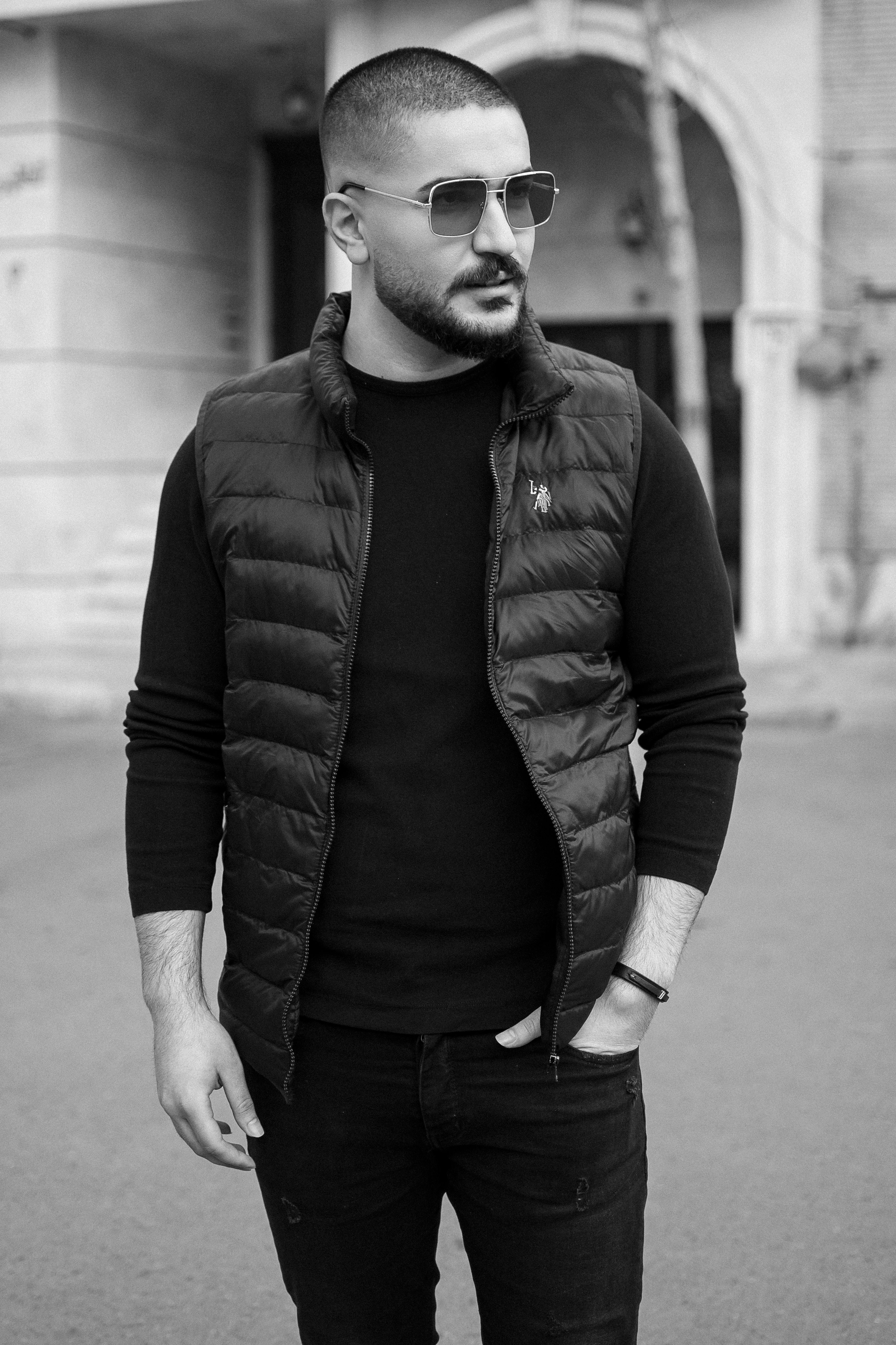 Monochrome portrait of a fashionable man in urban setting wearing sunglasses and puffer vest.
