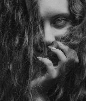 A captivating black and white portrait of a woman with curly hair partially covering her face.
