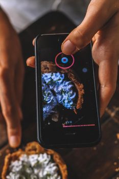 Close-up of hands taking a photo of a dessert with a smartphone.