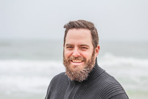 Man Wearing Black Zip-up Jacket Near Beach Smiling at the Photo