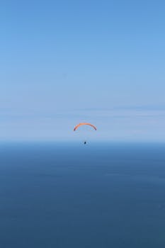 A lone paraglider enjoys a thrilling flight over a vast open sea under a clear blue sky.