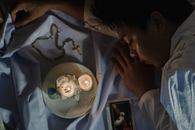 Crop ethnic believer resting on textile with flaming candles