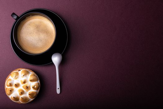 Top view of a coffee cup and pastry on a purple textured background with copy space.