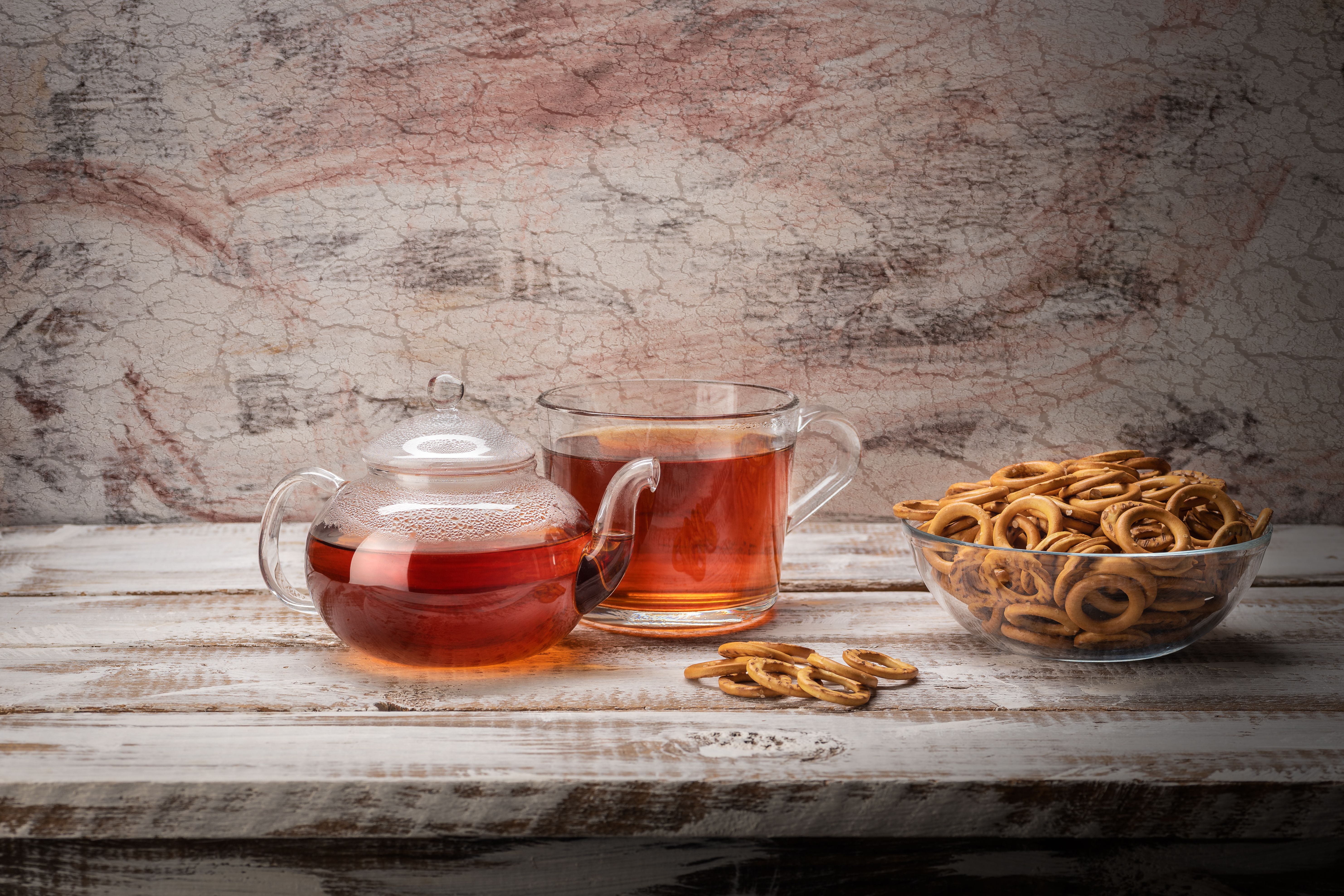Warm amber tea in transparent glass with dried herbs on dark wooden surface