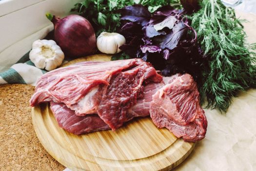 Close-up of raw beef on a wooden board with fresh herbs and vegetables.