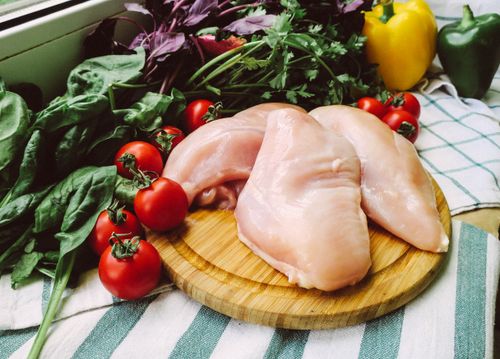 Free Raw chicken breasts on chopping board surrounded by fresh vegetables for cooking inspiration. Stock Photo