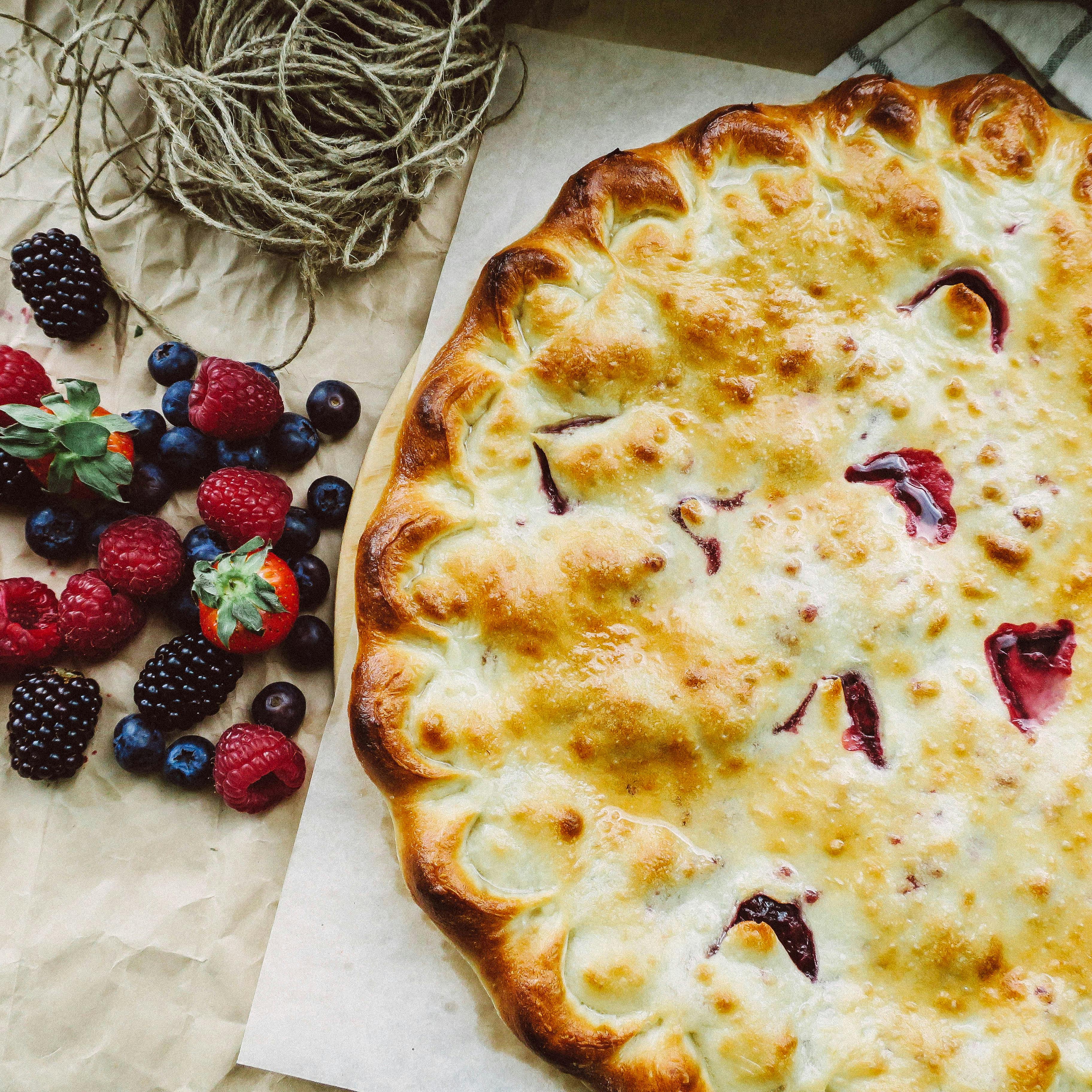 Delicious homemade berry pie with a golden crust accompanied by fresh berries, perfect for a rustic kitchen setting.