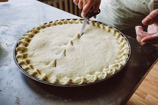 Hands skillfully trimming homemade pie crust with scissors in a kitchen setting.