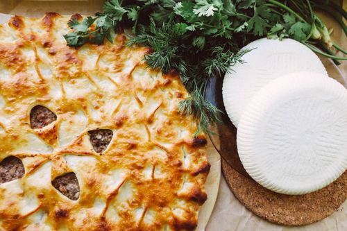 Free Savory baked cheese pie with a golden crust, accompanied by fresh herbs and cheese wheels. Stock Photo