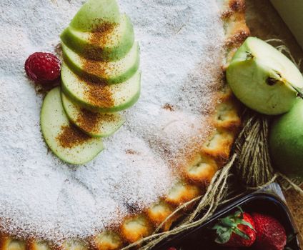 Top view of homemade apple pie dusted with sugar and surrounded by fresh fruits, perfect for dessert lovers.