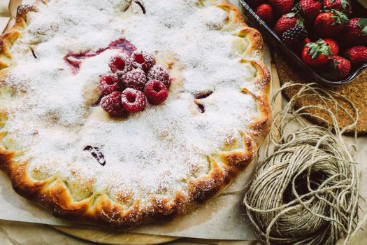 Delicious homemade raspberry pie dusted with powdered sugar, surrounded by fresh strawberries.