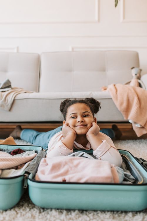 Free Young girl lying on suitcase in living room, smiling, showcasing travel preparations. Stock Photo