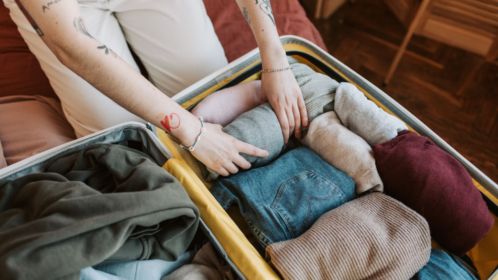 A person placing folded clothes in an open suitcase