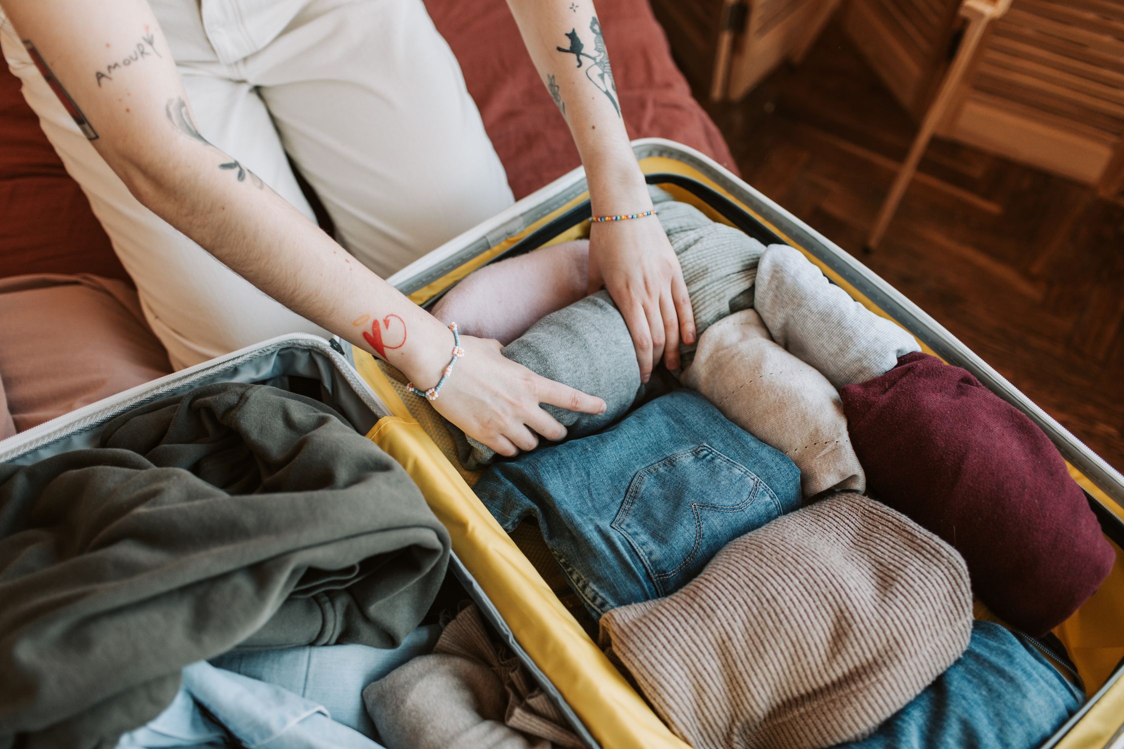 Woman packing neatly folded clothing items into an open suitcase on a bed