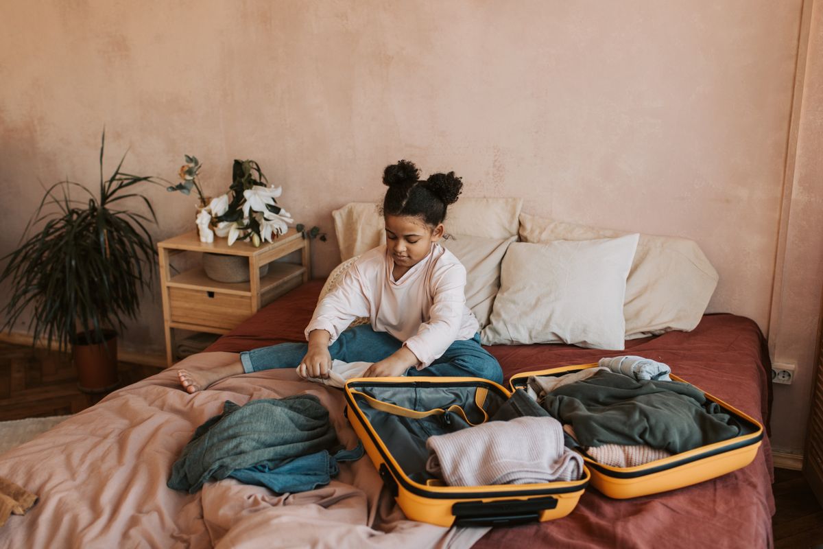 A child packing clothing into a suitcase before a family trip