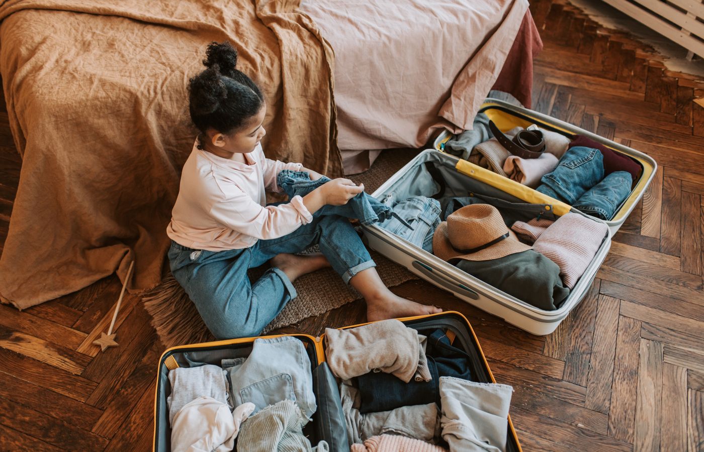 Young child sitting on bed packing a suitcase for an upcoming family vacation.