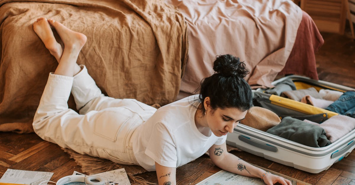 Woman lying on floor in bedroom, planning trip with map and open suitcases.