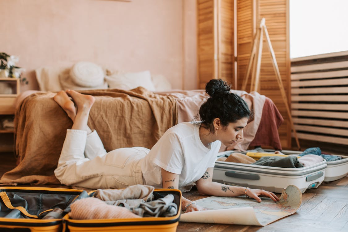 Free Woman Lying on the Floor and Looking at a Map with Open Suitcases  Stock Photo