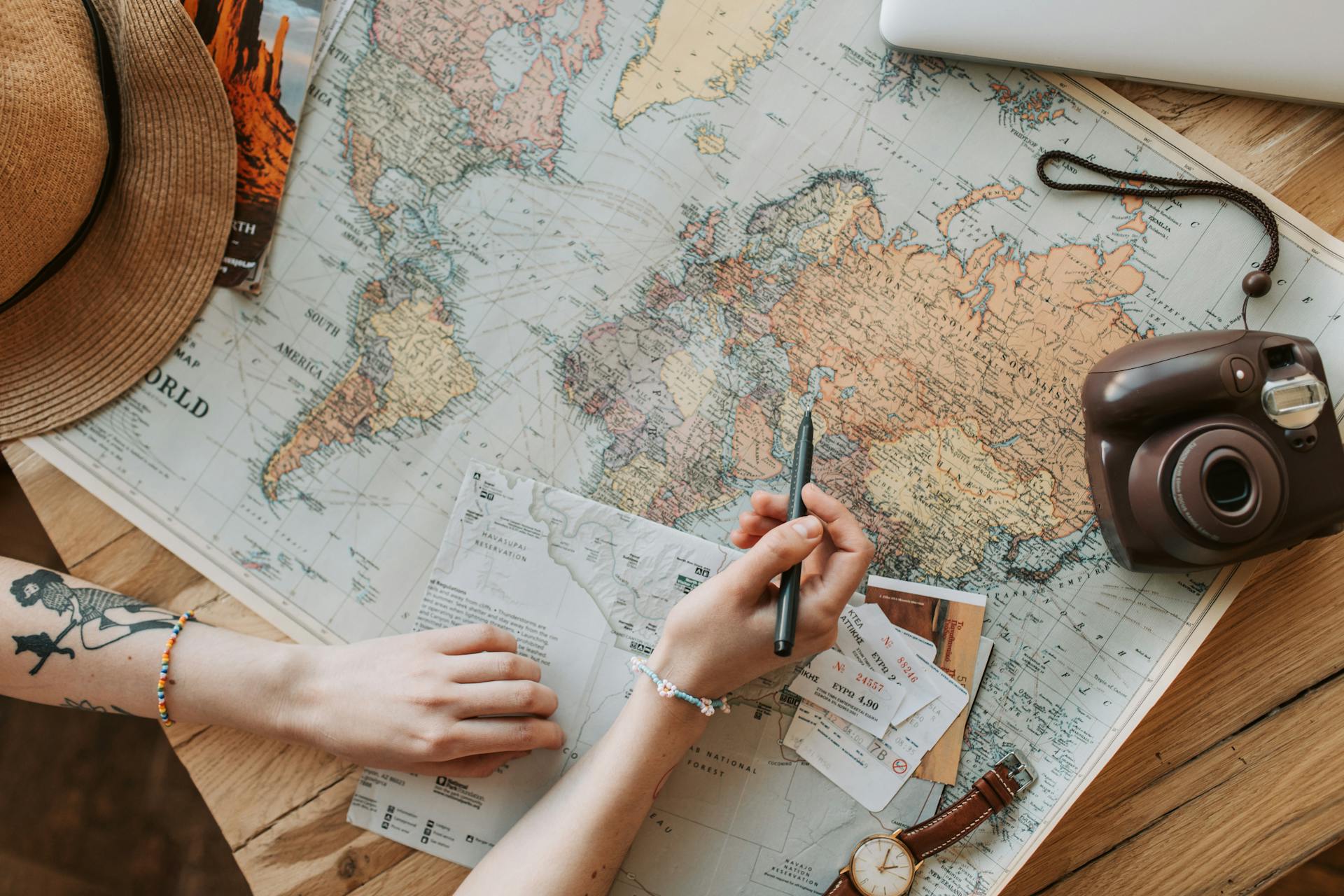 Top view of a woman's hands planning a trip with a map, camera, and travel items.