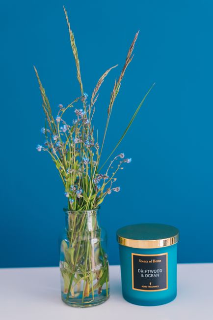 Stylish decoration with glass vase and candle on blue background.