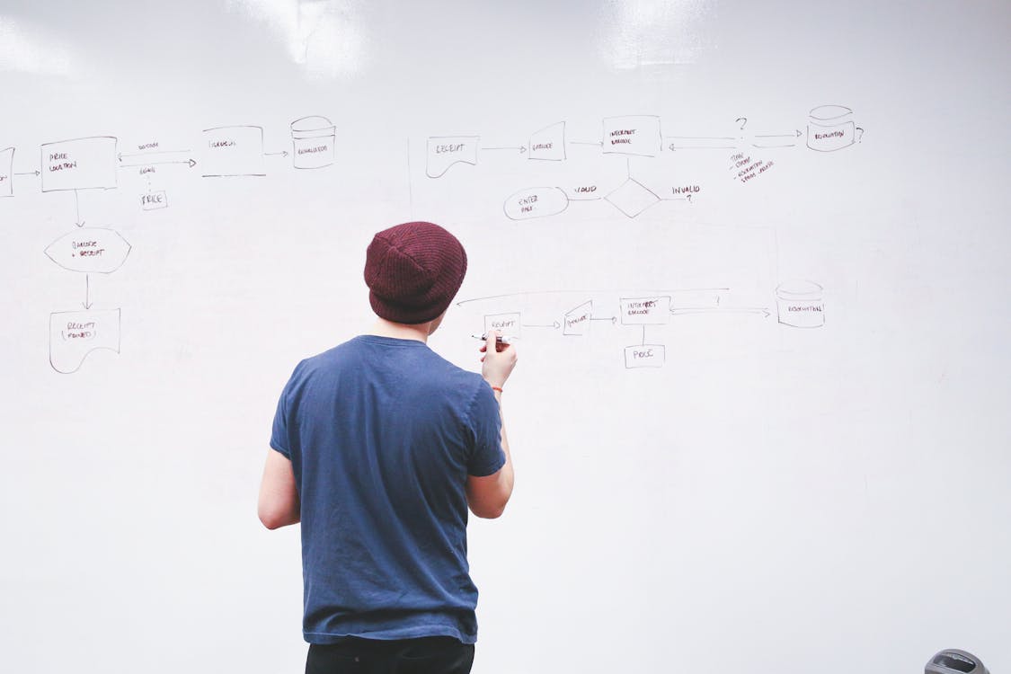 Man Standing While Holding Red Marker Pen Facing Marker Board