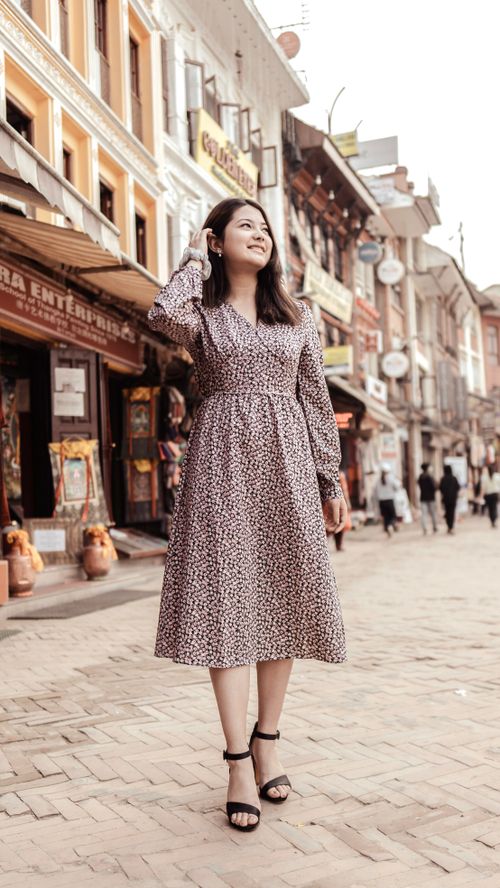 Free A stylish woman in a floral dress smiles while walking on a bustling city street. Stock Photo