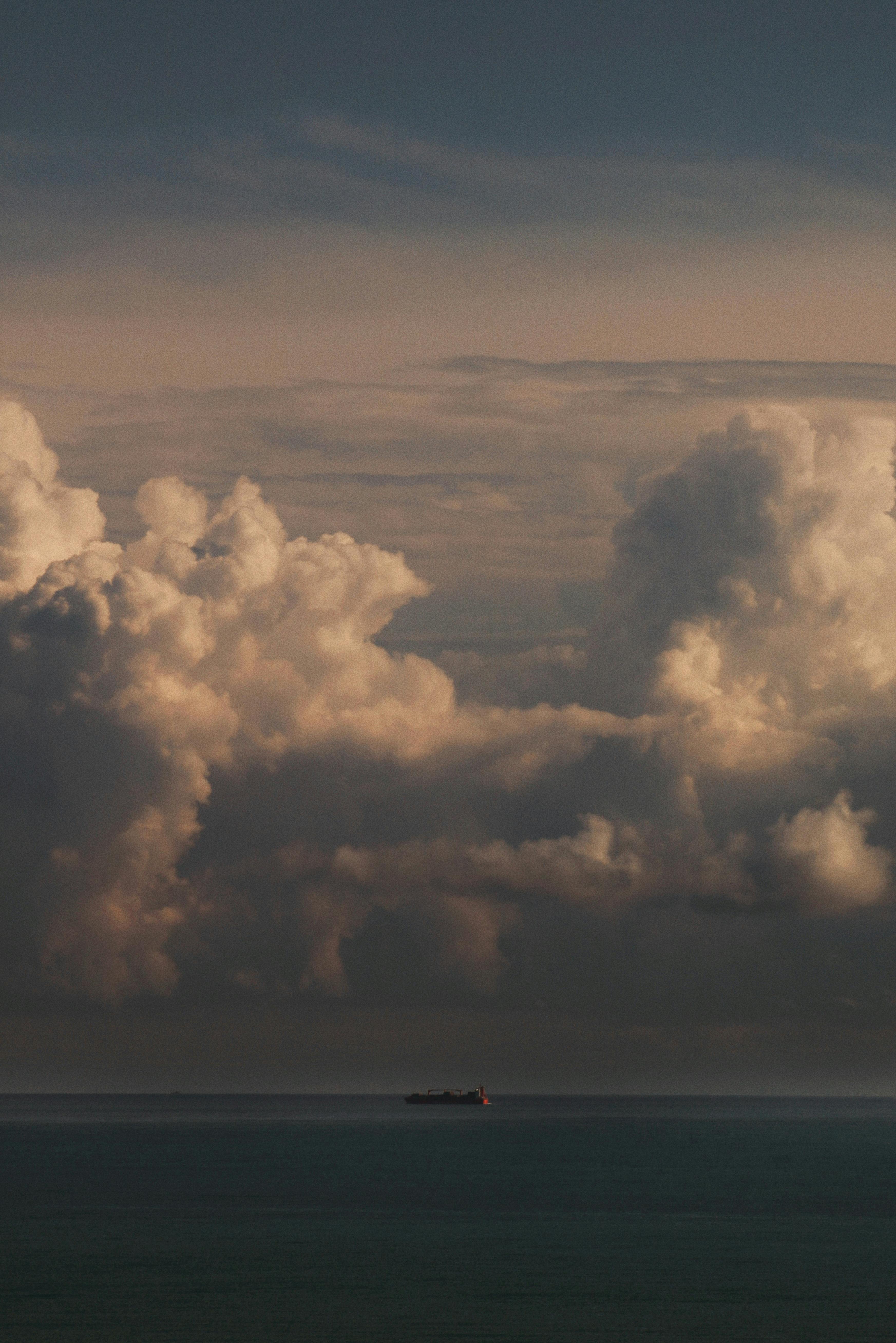 A serene ocean view with majestic clouds and a solitary ship at sunset, creating a peaceful yet dramatic scenery.